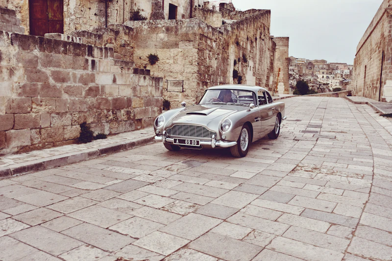 A silver Aston Martin DB5 on a stone-paved old town street