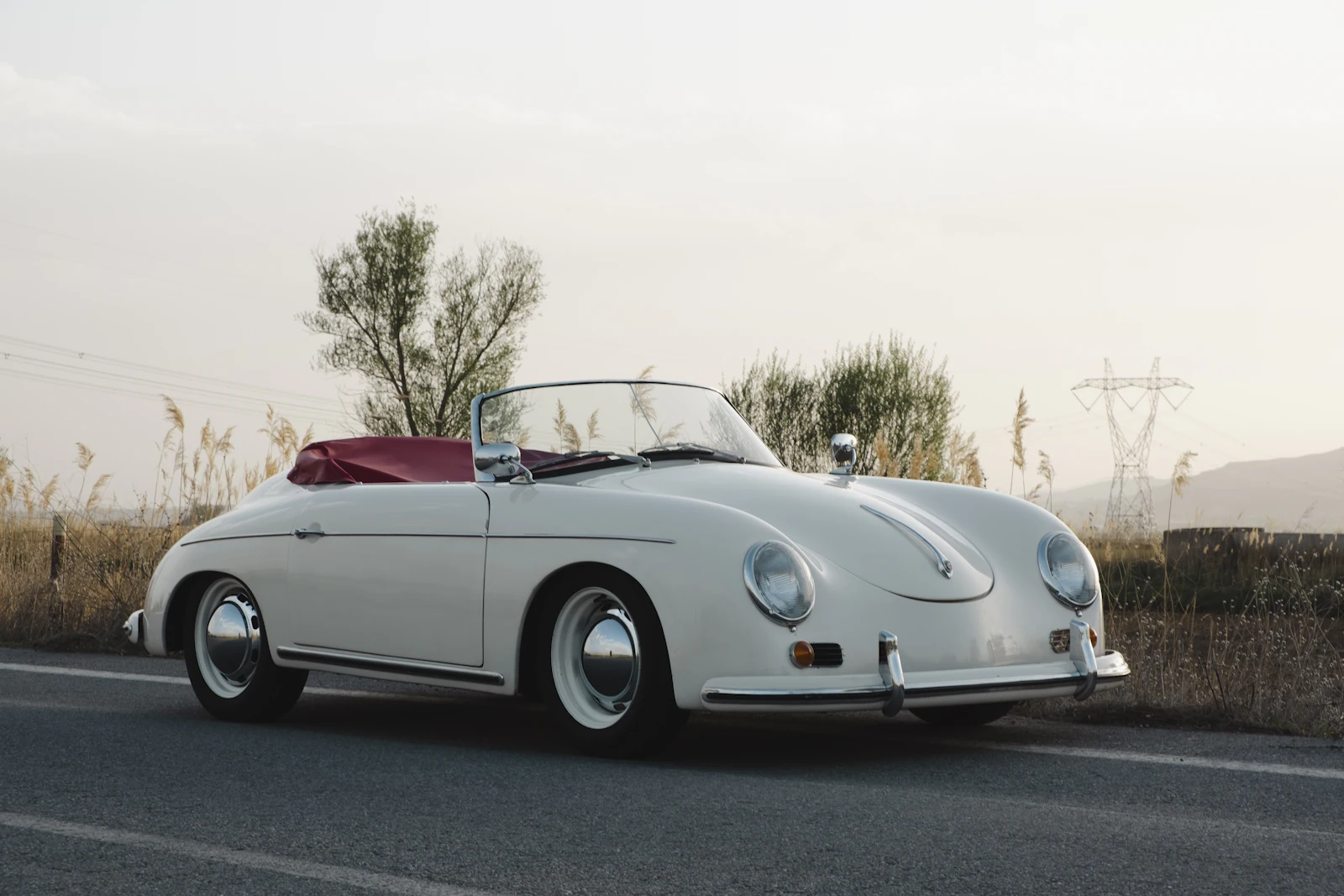 A white Porsche 356 Speedster with a red interior on a quiet country road