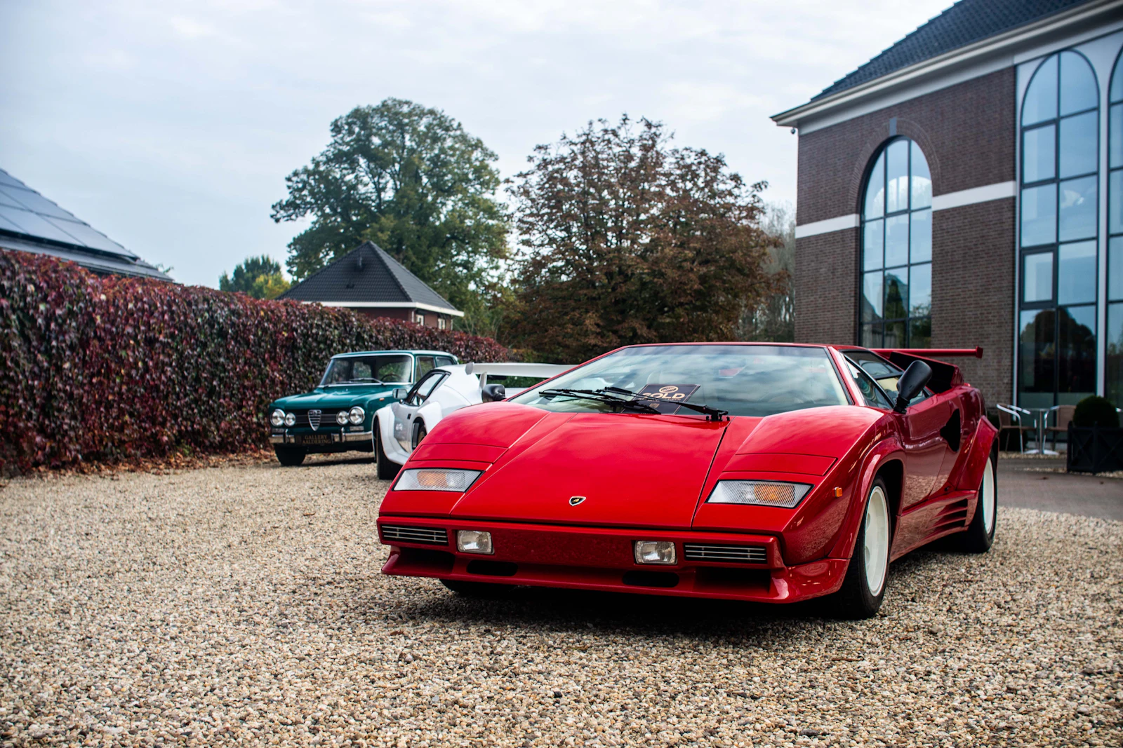 A red Lamborghini Countach on a gravel drive in front of a brick building